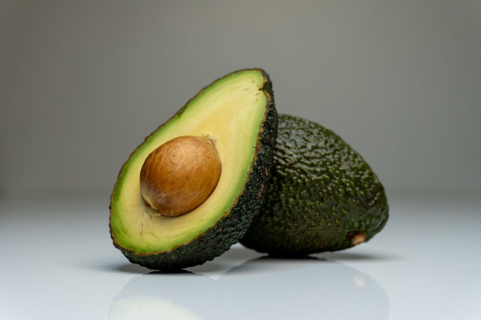 Avokado Faydaları: Besin Değeri ve Doğru Tüketim Önerileri 1 Close-up of a halved avocado with seed, showcasing vibrant colors on a reflective white background.