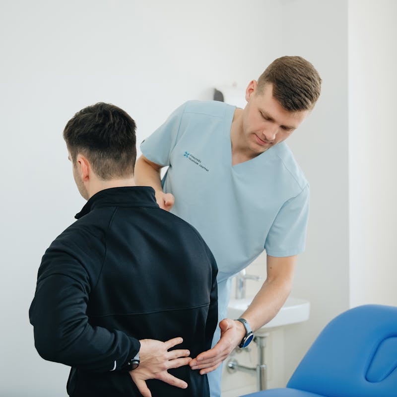 Bel Ağrısı Neden Olur? Yaygın Nedenler ve Tedavi Rehberi 3 Fizyoterapist klinikte hastanın sırtına manuel terapi uyguluyor