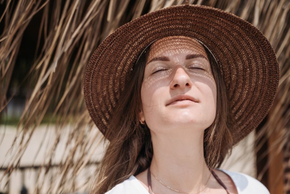 Güneş Yanığına Ne İyi Gelir? Cilt Tahrişine Karşı Doğal Çözümler 1 Close-up portrait of a woman with eyes closed, wearing a sunhat, enjoying sunlight.